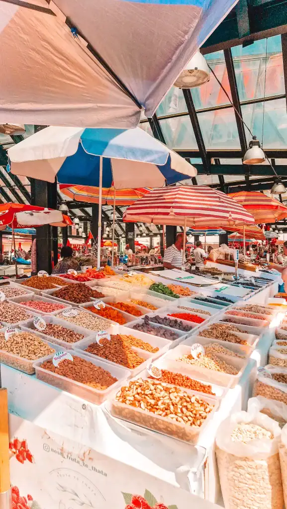 A colorful market scene filled with bins of dried fruits, nuts, and seeds under vibrant umbrellas, buzzing with energy and local shoppers.