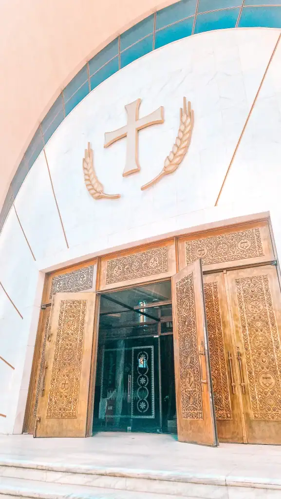 Ornate golden doors of Tirana’s Resurrection of Christ Orthodox Cathedral, set in a grand white marble arch with a large cross above the entrance.