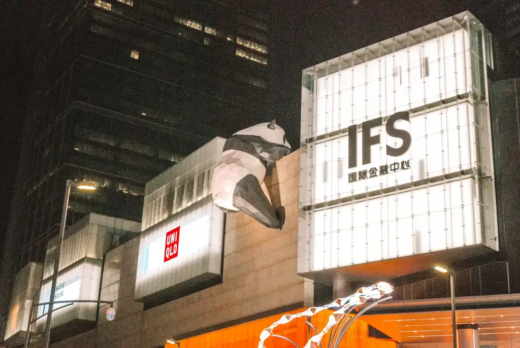 A giant panda sculpture climbs the IFS mall facade in Chengdu, China, with the bright signage of UNIQLO and other shops visible at night.