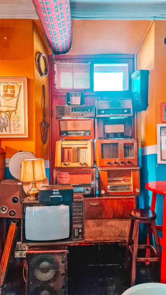 Wall of vintage radios and retro tech stacked inside Radio Bar in Tirana, set against bold colors and moody lighting. One of the best cafés in Tirana for vintage lovers and creative souls.
