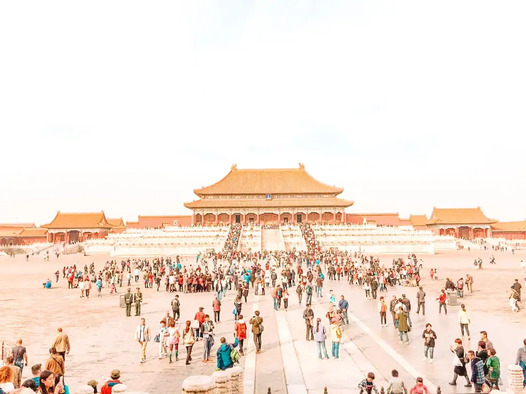 A wide-angle view of the Forbidden City in Beijing, filled with visitors walking through the massive courtyard toward the historic palace.
