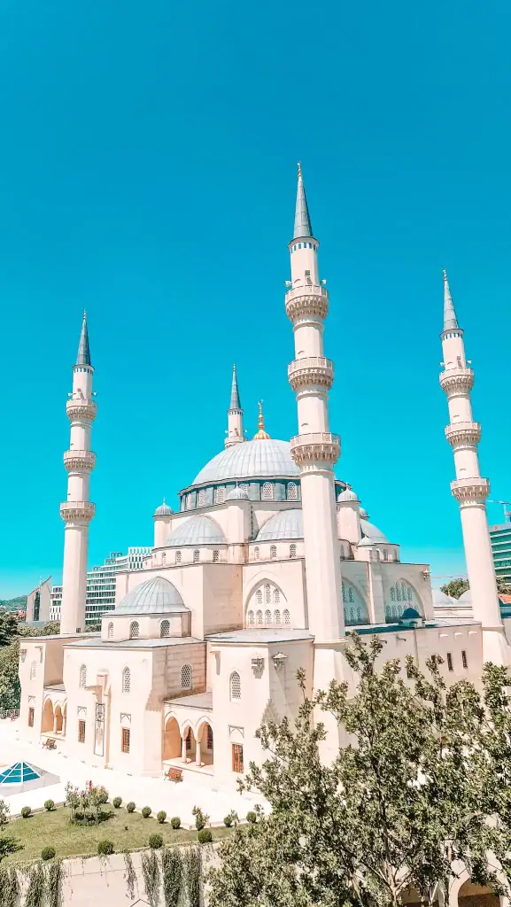 A stunning close-up of the Grand Mosque’s detailed architecture with four tall minarets and cascading domes, glowing under the summer sun in central Tirana.