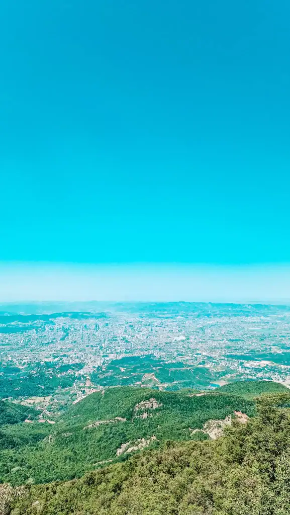 A breathtaking panoramic view from Dajti Mountain showing the sprawling city of Tirana nestled between green hills—one of the best vistas during 2 days in Tirana.