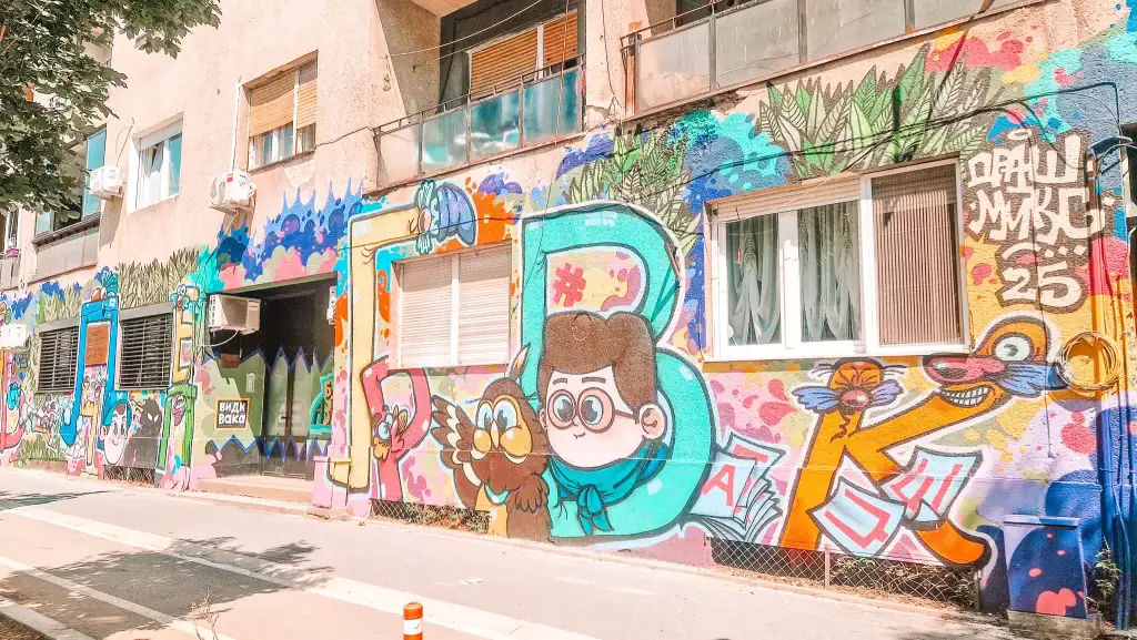 Colorful street mural on a building in Skopje’s Debar Maalo neighborhood, with cartoon characters and bold graffiti art outside local cafés.