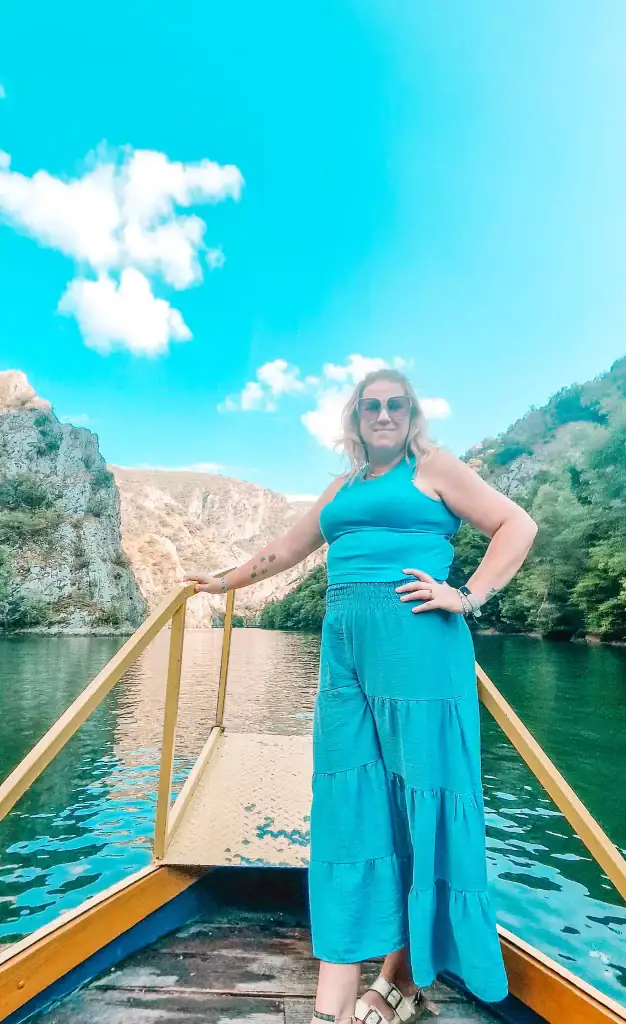 Em stands confidently at the front of a yellow boat cruising through Matka Canyon, wearing a blue outfit that matches the vibrant turquoise water and clear sky.