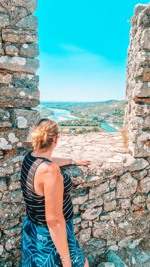 Framed by ancient stone walls, Em gazes at the winding Buna River and green landscape below from a high vantage point at Rozafa Castle.