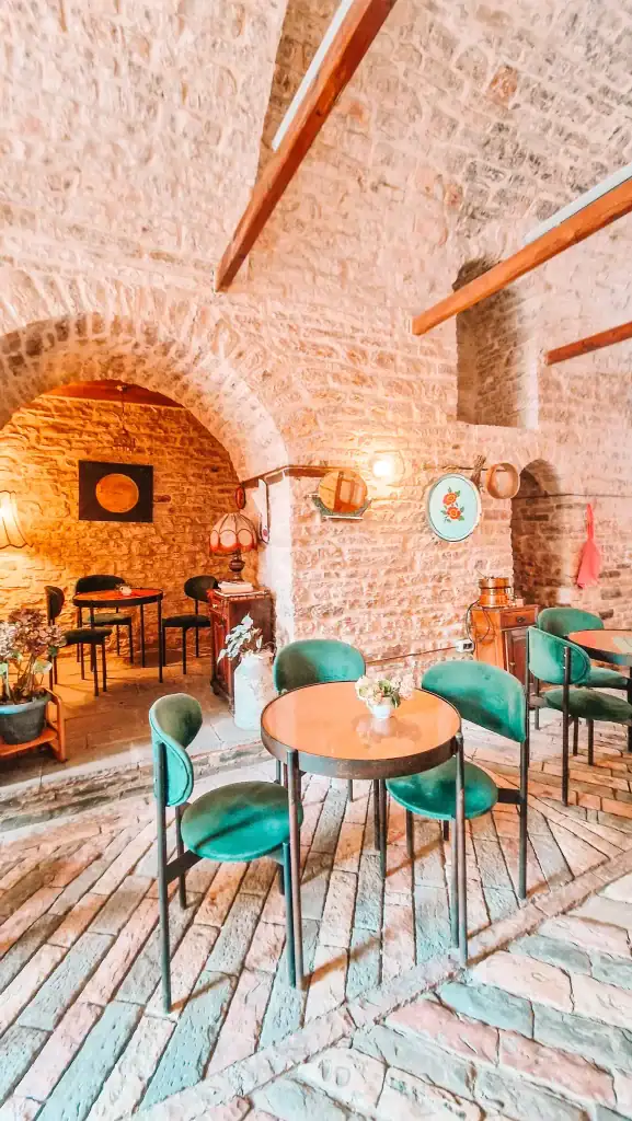 Interior of a traditional café in Gjirokaster with exposed stone walls, green velvet chairs, and soft lighting that gives a warm and intimate vibe perfect for a relaxed meal or drink.