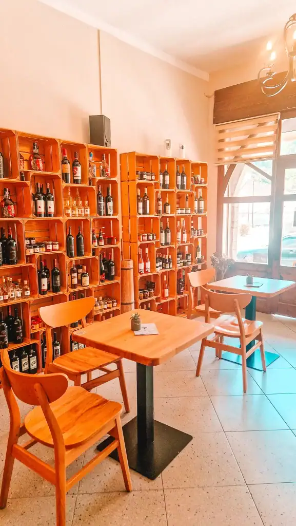 Cozy shop interior with wooden shelves filled with wine bottles, spirits, and preserves, and simple wooden tables and chairs for tastings.