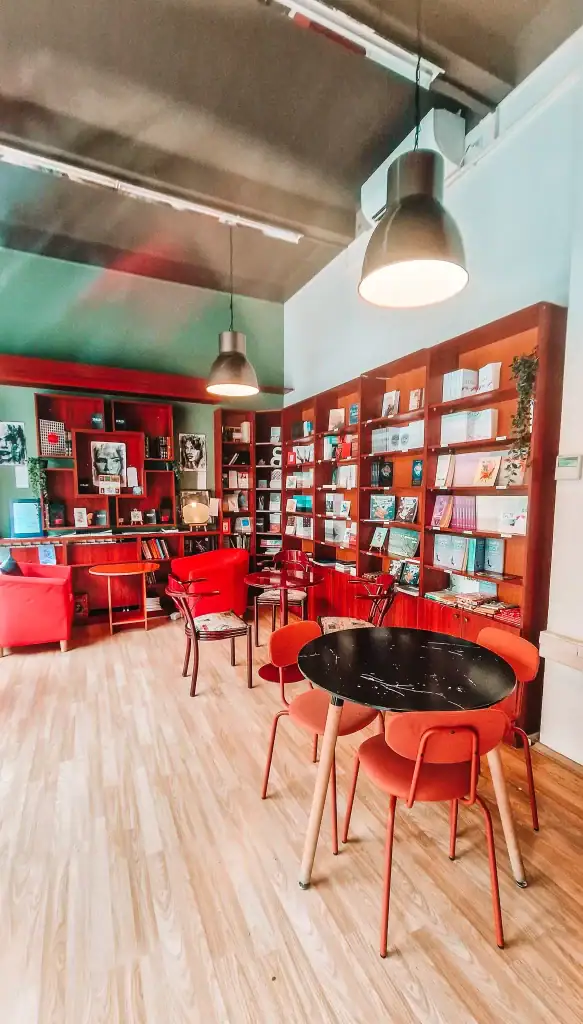 The cozy reading area of a Skopje book cafe, with red and orange chairs, black round tables, and bookshelves filled with literature and local art.