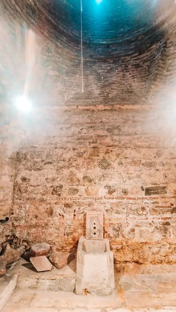 A stone-walled chamber with a small basin and spout structure, part of a hammam, a historic bath or ritual cleansing area preserved inside a Skopje museum.