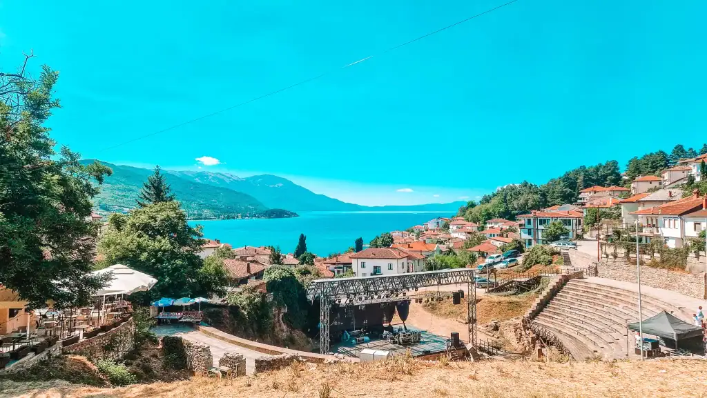 Panoramic view over Lake Ohrid and the red-roofed town below, with a Roman amphitheatre nestled in the hillside, blending culture, nature and history in North Macedonia.