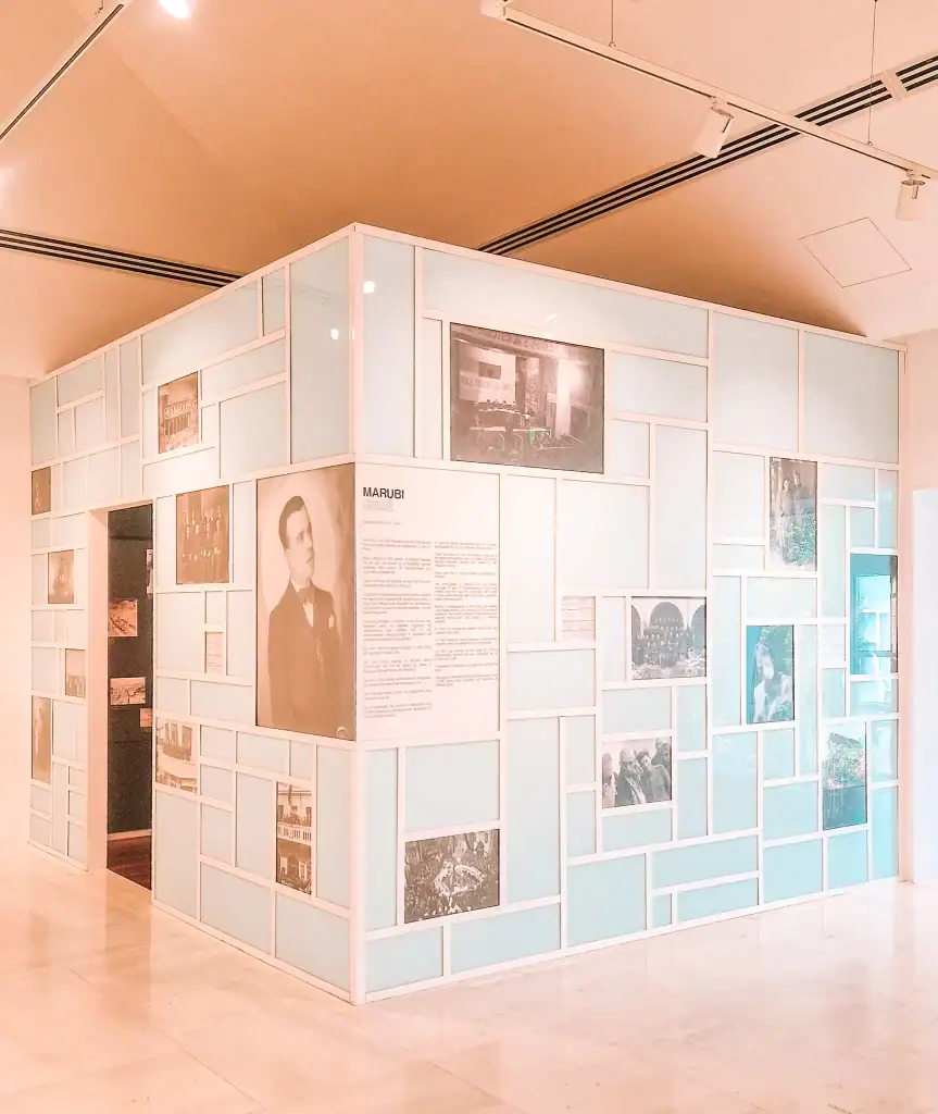 A modern gallery installation at Marubi Museum in Shkoder, featuring light blue panels with framed historical photographs and text highlighting local photographic history.