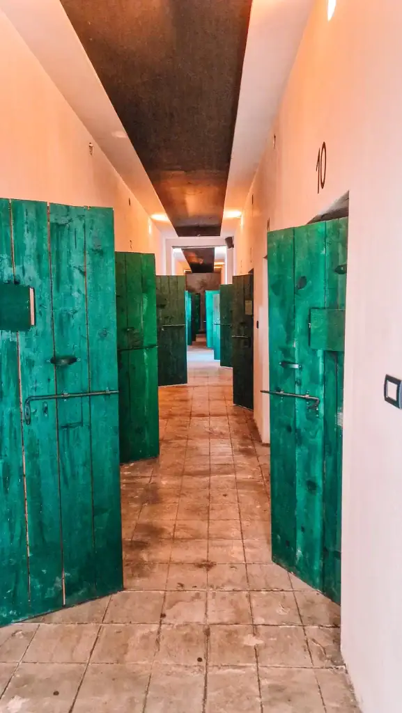 Dimly lit hallway with aged green wooden cell doors at the Site of Witness and Memory in Shkoder, once a political prison during communist rule.