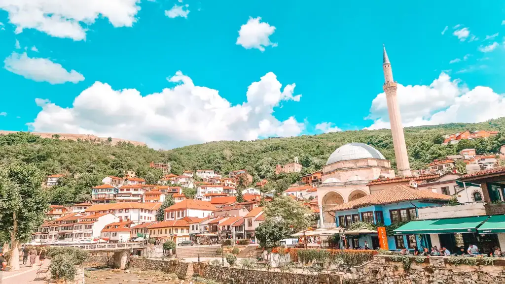 A panoramic view of Prizren’s Old Town with the Sinan Pasha Mosque and its tall minaret surrounded by red-roofed homes. The lively riverfront cafes are popular stops on day trips from Skopje.
