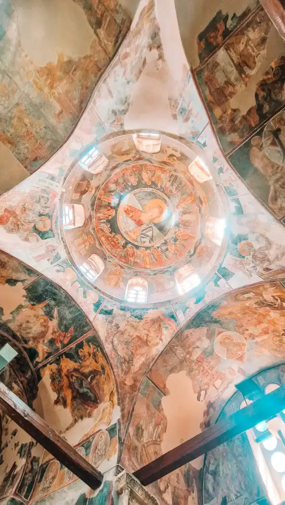 A domed ceiling inside a historic Orthodox church in Skopje, richly decorated with fading frescoes and a central icon of Christ surrounded by saints.