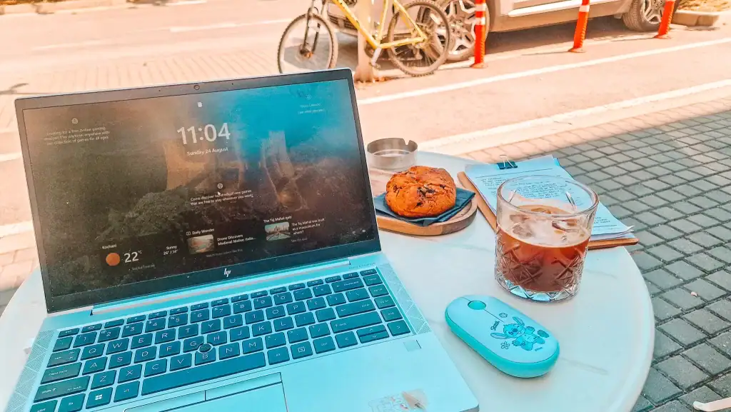 Outdoor café table in Skopje with a laptop, iced coffee, and a pastry, showing a relaxed work-friendly spot with bikes and cars in the background.