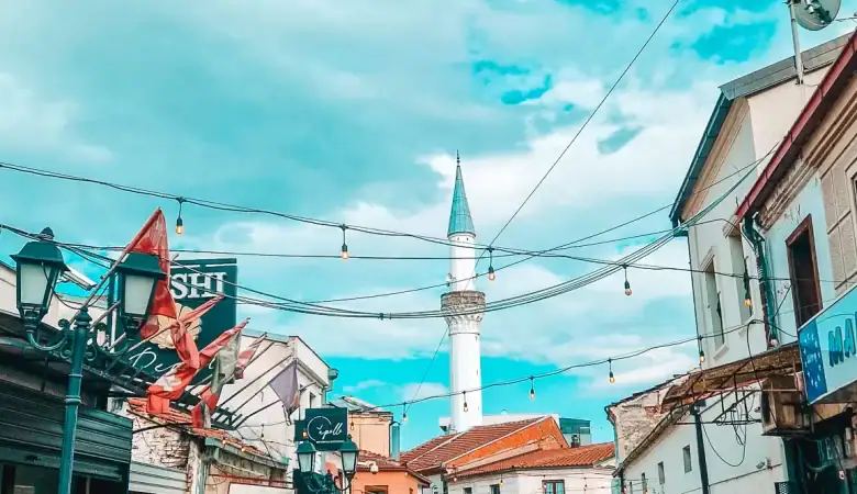 Bustling street in Skopje’s Old Bazaar featuring shops, hanging lights, and a tall mosque minaret rising above the historic cobblestone lane.