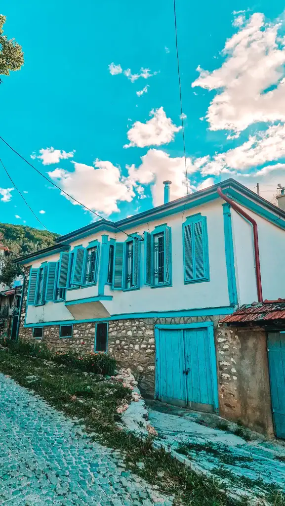 Charming stone-and-plaster house with turquoise shutters and doors, situated on a steep cobbled street in Krusevo, perfect for those exploring off-the-beaten-path things to do in Krusevo.