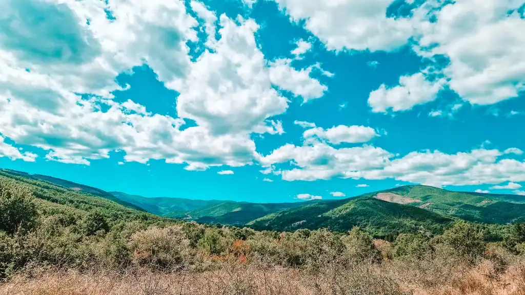 Expansive view of green rolling mountains under a bright blue sky filled with fluffy white clouds, capturing the natural beauty ideal for hiking and exploring things to do in Krusevo.
