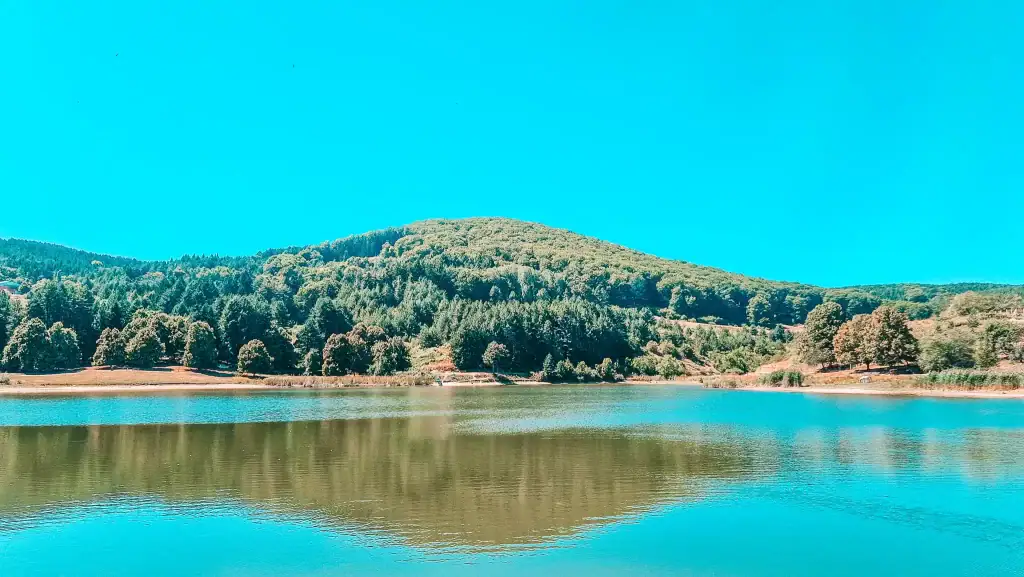 Tranquil lake surrounded by forested hills and reflecting a clear blue sky, offering a peaceful nature retreat and a relaxing outdoor option among things to do in Krusevo.