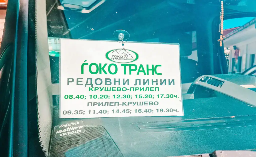 Close-up of a bus timetable for Goko Trans displayed inside a vehicle window, listing regular route times between Krusevo and Prilep in Macedonian Cyrillic script.