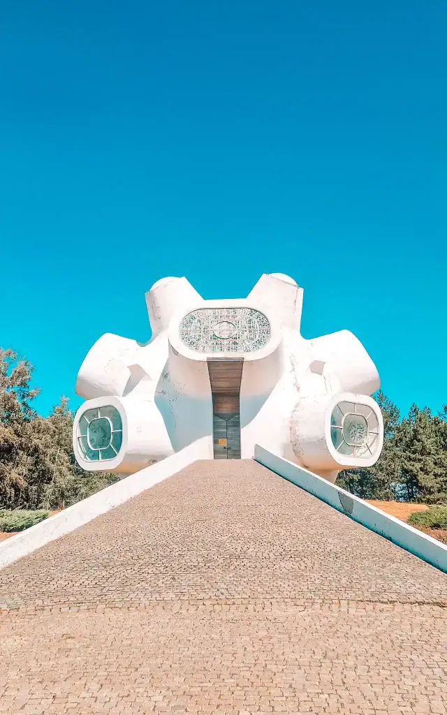 Close-up of the bold, sculptural design of the Makedonium monument, with circular stained-glass windows and a steep stone ramp leading to the entrance under a vivid blue sky.
