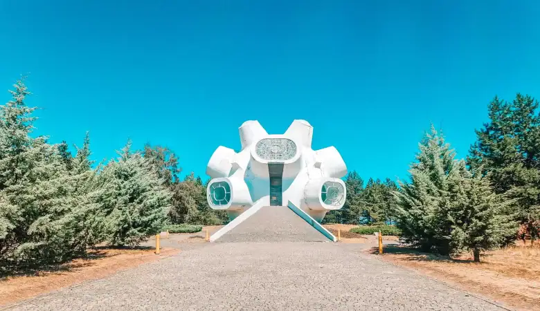 Wide-angle view of the futuristic white Makedonium monument in Krusevo, surrounded by trees and accessed by a stone path, one of the most iconic things to do in Krusevo.