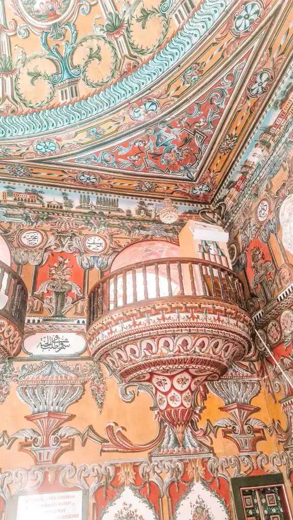 Close-up of the Painted Mosque interior in Tetovo, North Macedonia, showing vividly coloured floral murals, calligraphy, and carved wooden balconies in striking Ottoman-Baroque style.