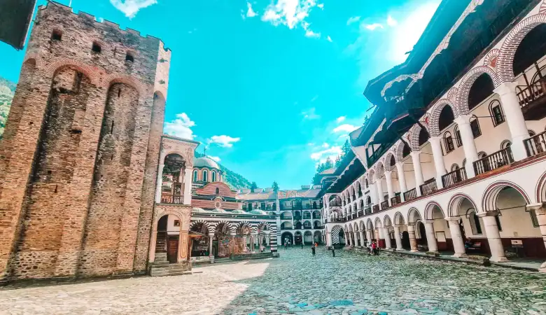 View of the medieval Hrelyo Tower at Rila Monastery, surrounded by monastic buildings with archways and decorative balconies.