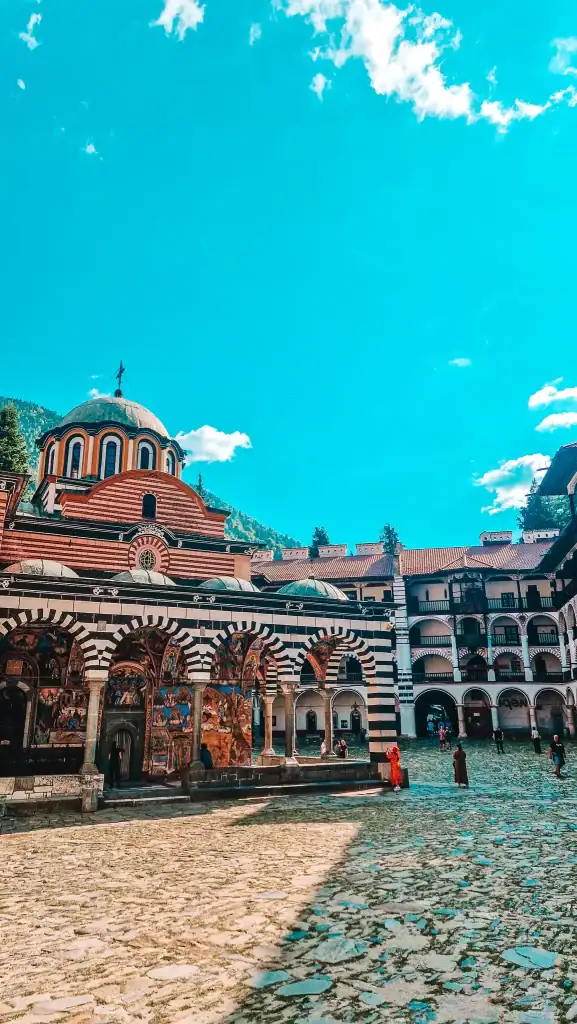 The colourful striped arches and intricate frescoes of Rila Monastery bask in the mountain sun as visitors stroll through the cobblestone courtyard. A must-visit for those exploring locations featured in books about Bulgaria’s religious and historical roots.