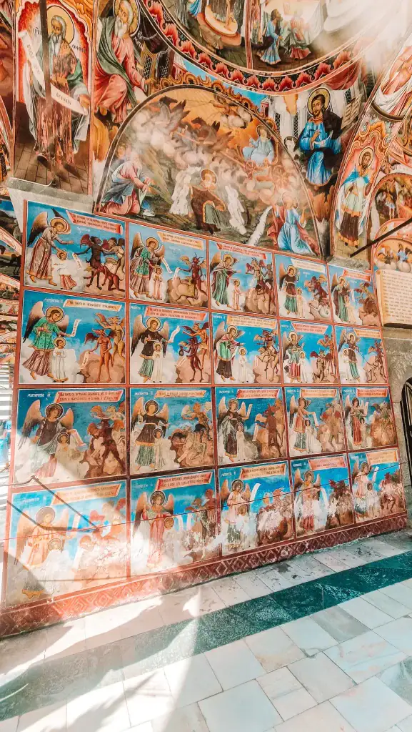 Colourful Orthodox frescoes on the outer wall of Rila Monastery, Bulgaria, depicting angels, saints, and dramatic biblical scenes in vibrant reds, blues, and golds.