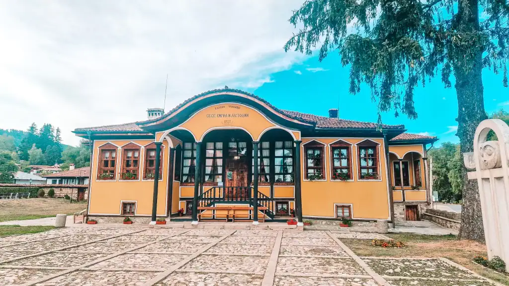 Wider view of the same 1837 school building under soft daylight, surrounded by cobblestone paths and blooming flowers. It’s a peaceful and educational stop among the many things to do in Koprivshtitsa.