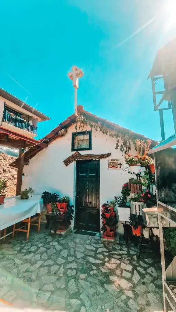 Small whitewashed Orthodox chapel in Ohrid, with a simple tiled roof, wooden door, and flower pots lining the cobbled courtyard.