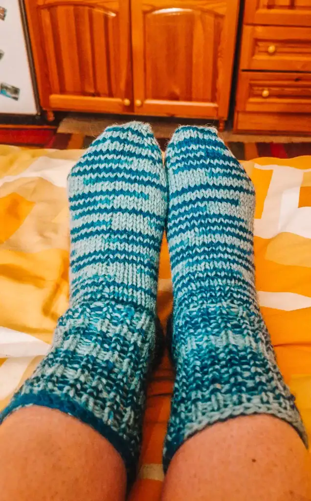 Em’s feet in cosy, blue striped hand-knitted socks resting on a warm bedspread, with wooden furniture in the background. A quiet moment to unwind after a full day exploring the charms of Koprivshtitsa.