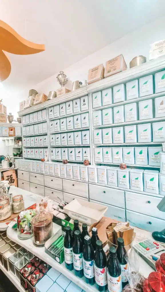A wall of silver tea canisters neatly stacked behind a counter with kombucha bottles, snacks, and tea accessories. The tea shop’s curated layout offers a break from Plovdiv’s coffee scene.