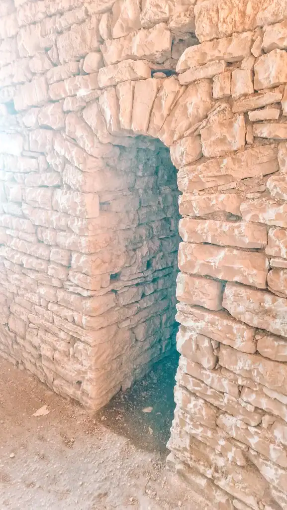 A narrow stone passageway framed by a rounded archway leads into a shadowy chamber. The rough, pale stones suggest an ancient or historical Albanian structure, possibly a castle or bunker.