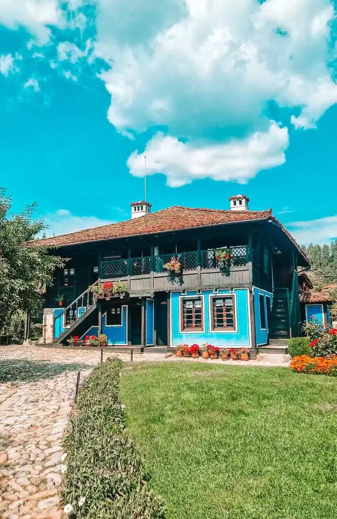 The bright blue wooden house of poet Dimcho Debelyanov in Koprivshtitsa, surrounded by flowers and cobblestones.