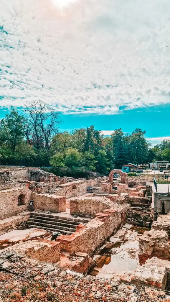 Ruins of the Roman bath complex in Hisarya, with stone arches and ancient walls surrounded by greenery.
