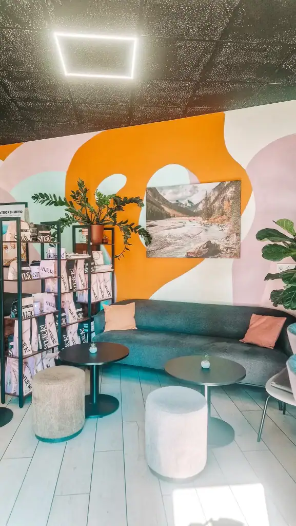A vibrant café interior in Plovdiv with bold abstract wall art, a comfy grey sofa, and shelves stacked with branded coffee bags—ideal for remote work with a splash of creativity.