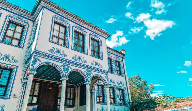 Close-up of a striking white and blue Plovdiv Revival house featuring symmetrical window designs and painted ornamentation.