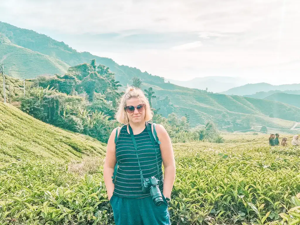 Em standing in a lush green tea plantation in the Cameron Highlands, surrounded by rolling hills and morning mist, a peaceful stop during a 2 week Malaysia itinerary.