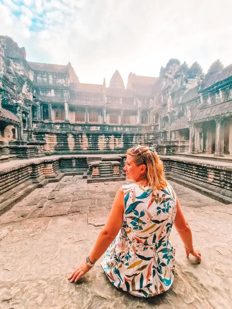 Em sits peacefully on the ancient stone floor of Angkor Wat’s inner courtyard in Cambodia, bathed in soft morning light as the temple walls rise behind her.