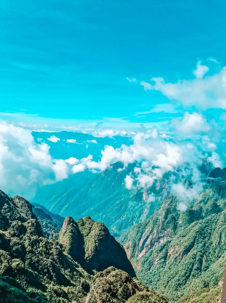 A breathtaking view of Vietnam’s rugged green mountain peaks from Fansipan, with fluffy clouds and blue sky stretching across the horizon.