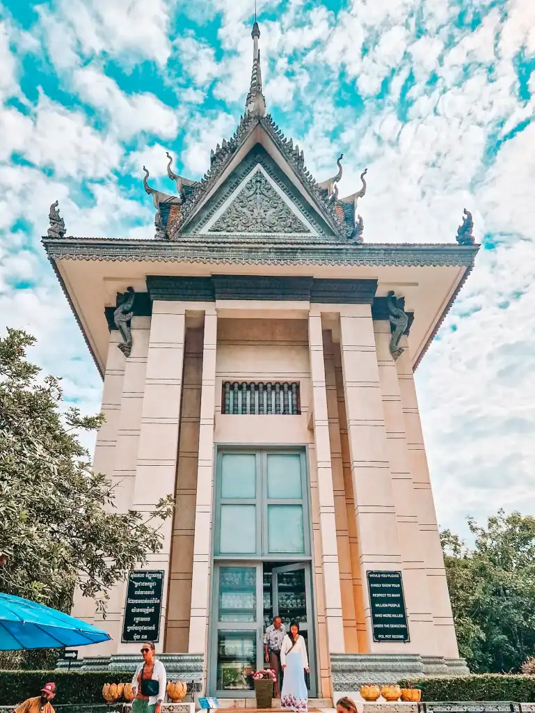 The Memorial Stupa at Choeung Ek Killing Fields in Phnom Penh, Cambodia, rises tall with traditional Khmer architecture, housing shelves of victims’ skulls behind glass as a tribute to those lost during the Khmer Rouge regime.