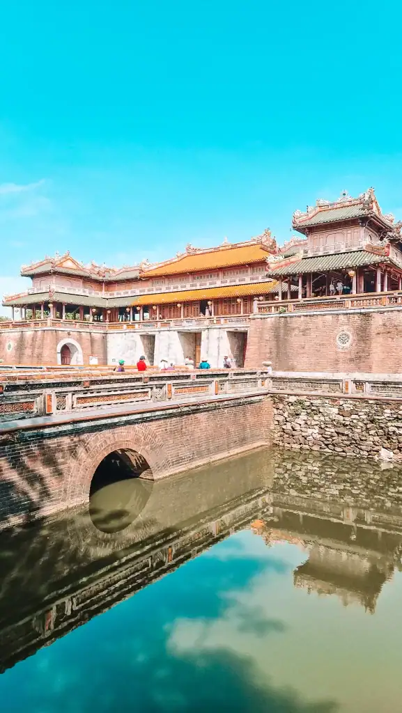 The grand entrance of the Imperial City in Hue, Vietnam, with ornate tiled roofs reflected perfectly in the still waters of the surrounding moat.