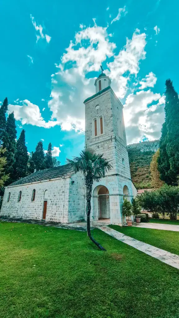 Stone Orthodox monastery with a bell tower set against a vivid blue sky and surrounded by greenery. Visiting this peaceful religious site is a lesser-known yet beautiful experience near Mostar.