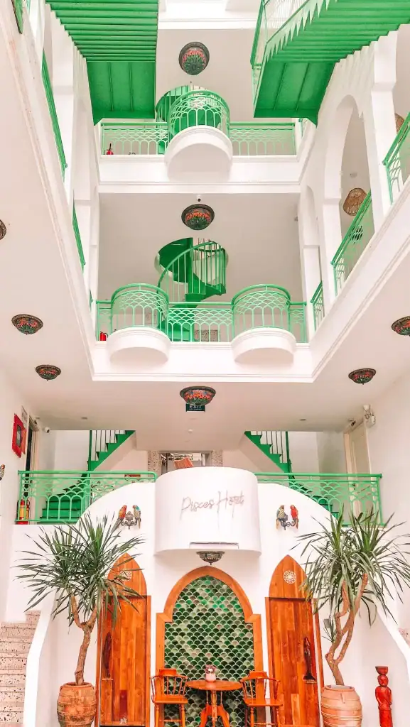 The bright and stylish interior of Pisces Hotel featuring bold green railings, spiral stairs, and arched wooden doors, with tropical plants adding to the vibrant atmosphere.