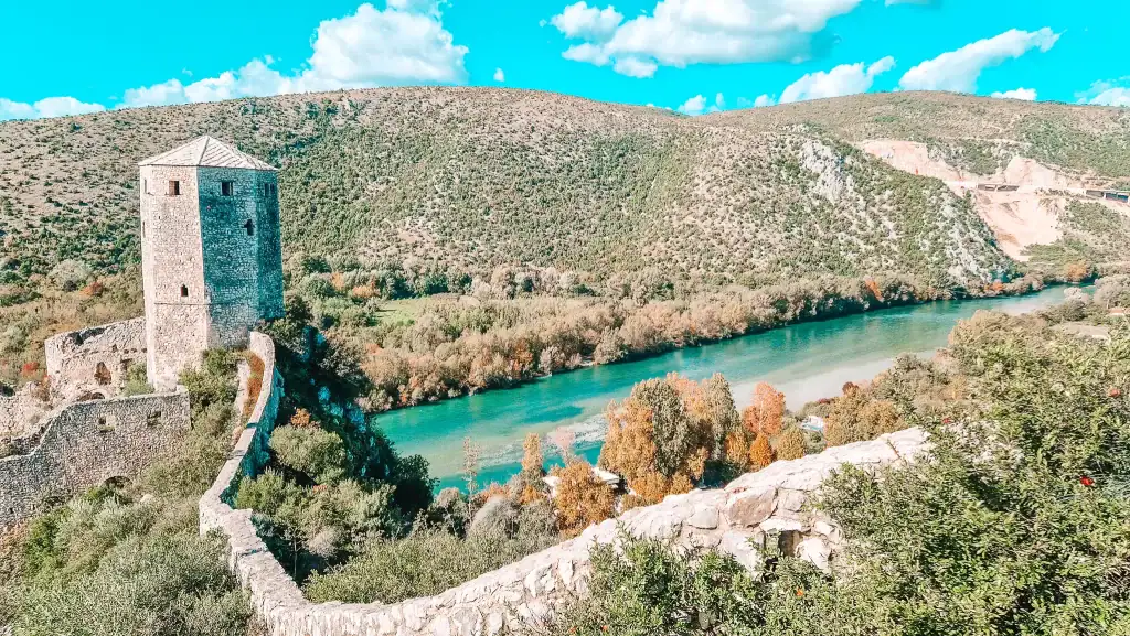 View of the historic Počitelj Fortress and its round stone tower overlooking the turquoise Neretva River and rolling hills. A panoramic highlight of things to do near Mostar for history and nature lovers.