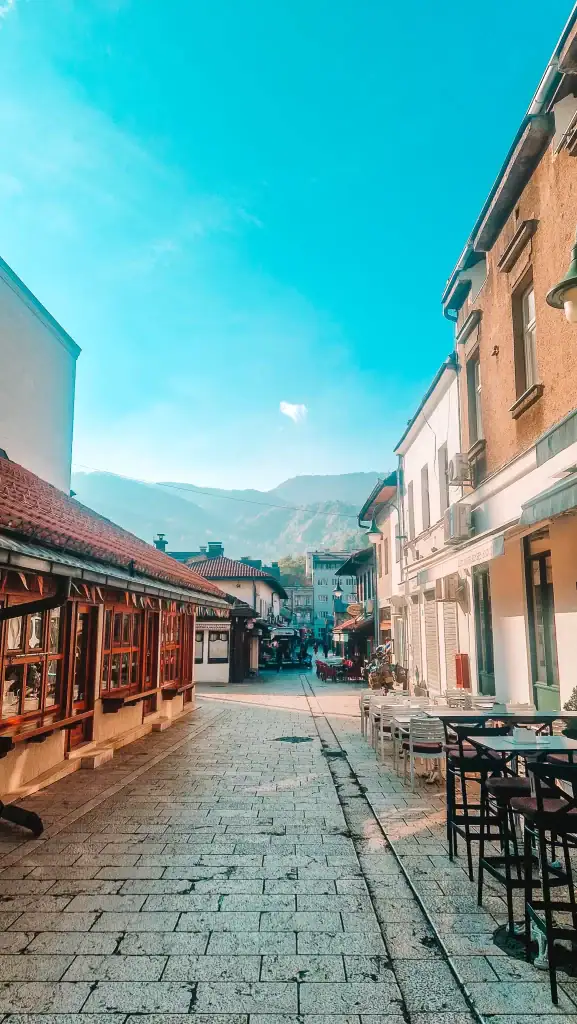 Quiet pedestrian street in Sarajevo’s old town with mountains in the distance, red-roofed buildings, and outdoor café seating. A charming place to wander, relax, and take in the city’s unique vibe.
