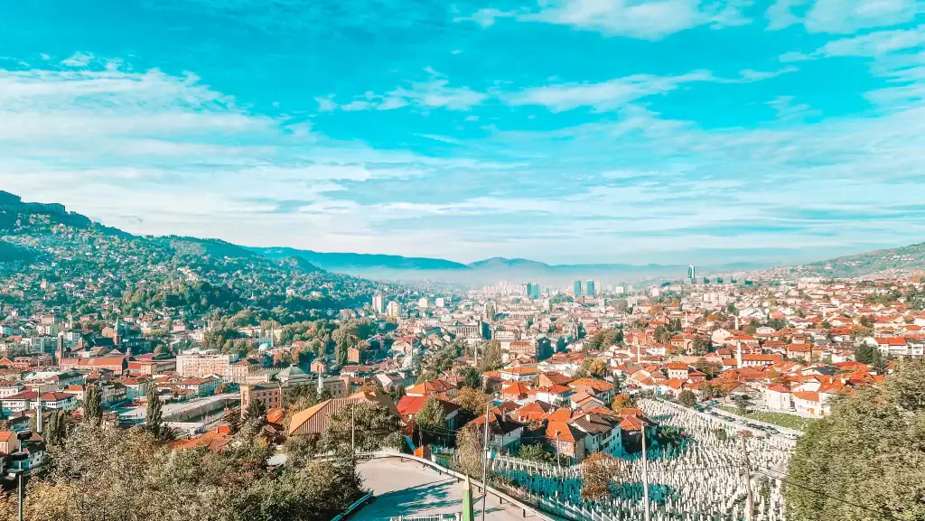Evening street scene in Sarajevo’s old town with shoppers, souvenir stalls, and restaurants lining both sides of a cobbled path. The golden-hour sky casts a soft glow, adding charm to this must-visit neighbourhood.